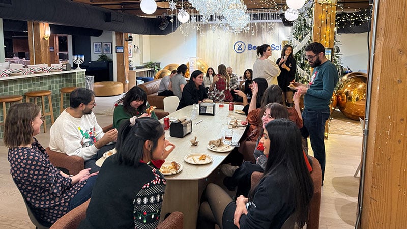 BenchSci employees gather around a long table sharing a meal in a festively decorated office.